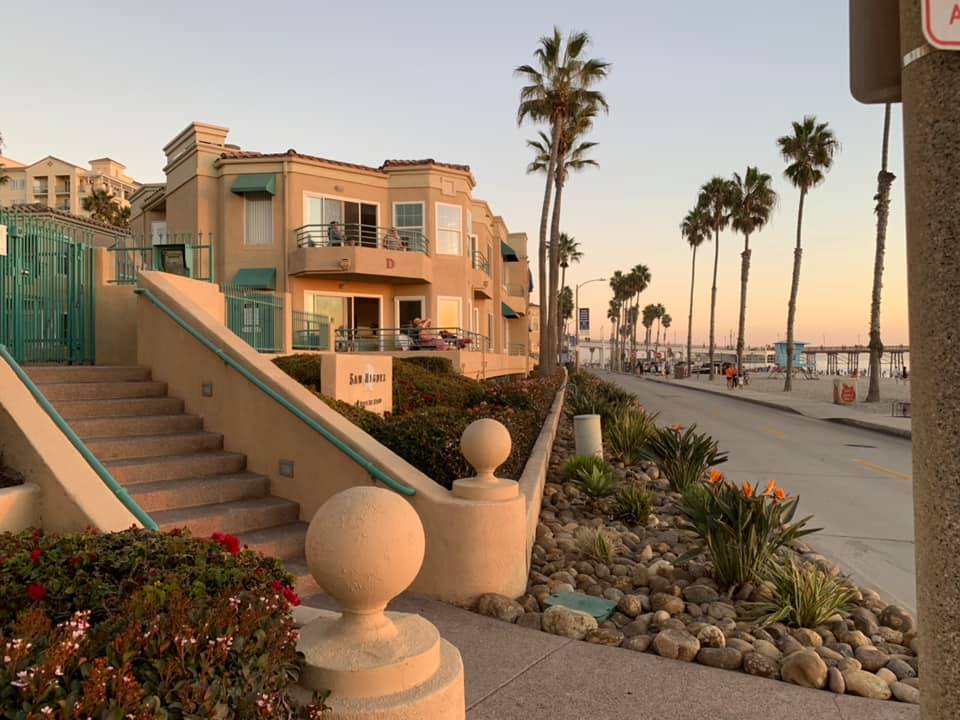 tan building up against a sidewalk lined with palm trees at sunset 