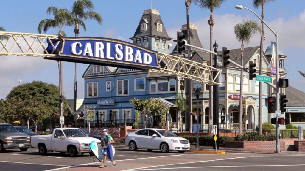 View of intersection featuring large Carlsbad sign above and a light blue Victorian house in the background.